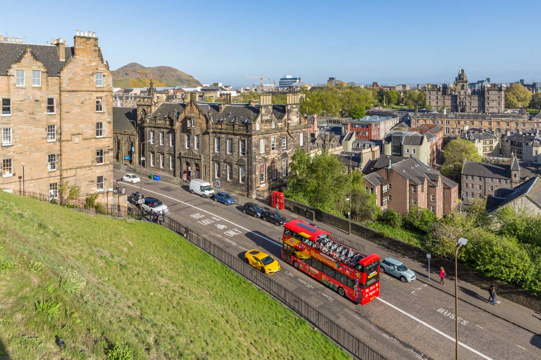 A high-angle photo showing a road with cars and an open-top bus driving down it in Edinburgh.