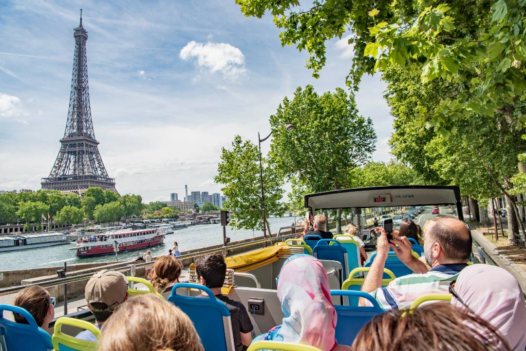 An open-top bus tour in Paris, the Eiffel Tower can be seen in the background.