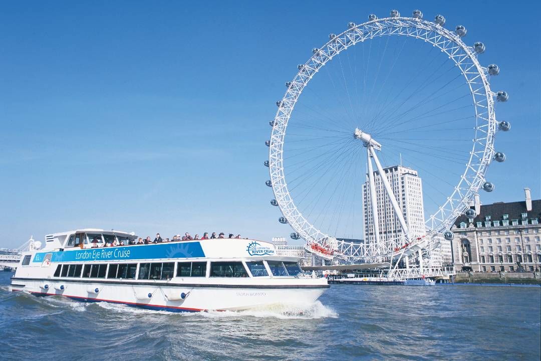 Photo of the London Eye with a river cruise passing it.