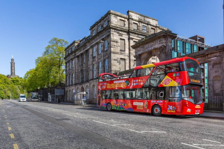 A red open-top hop-on hop-off Edinburgh bus tour driving down the street and passing by a building.