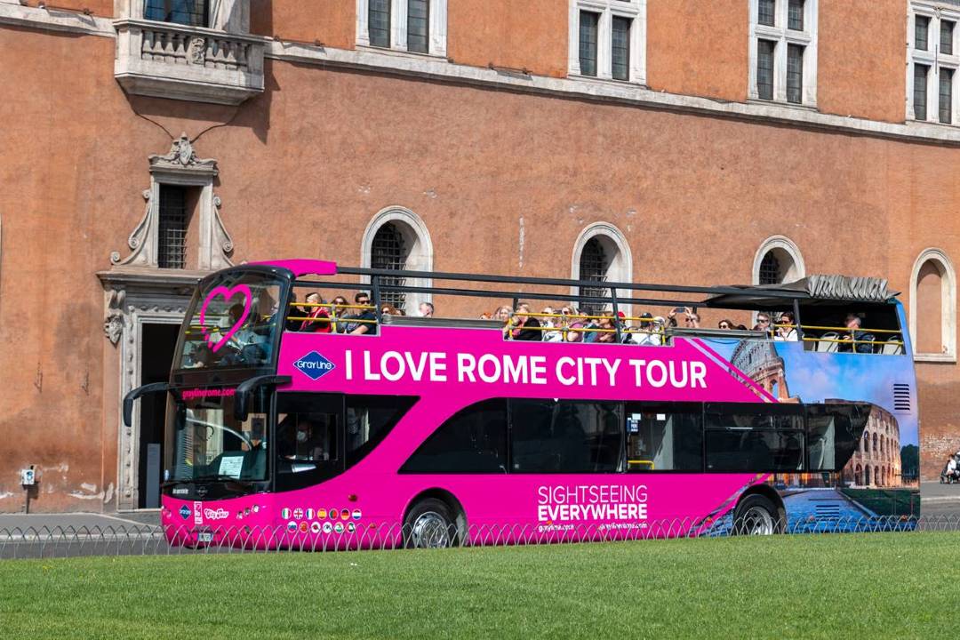 A pink hop-on hop-off Rome tour bus with the text 'I love Rome city tour' written on the side of it.