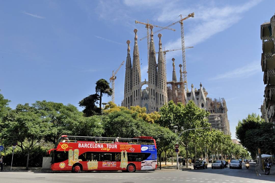 A Barcelona hop-on hop-off bus tour driving past Barcelona La Sagrada Familia.