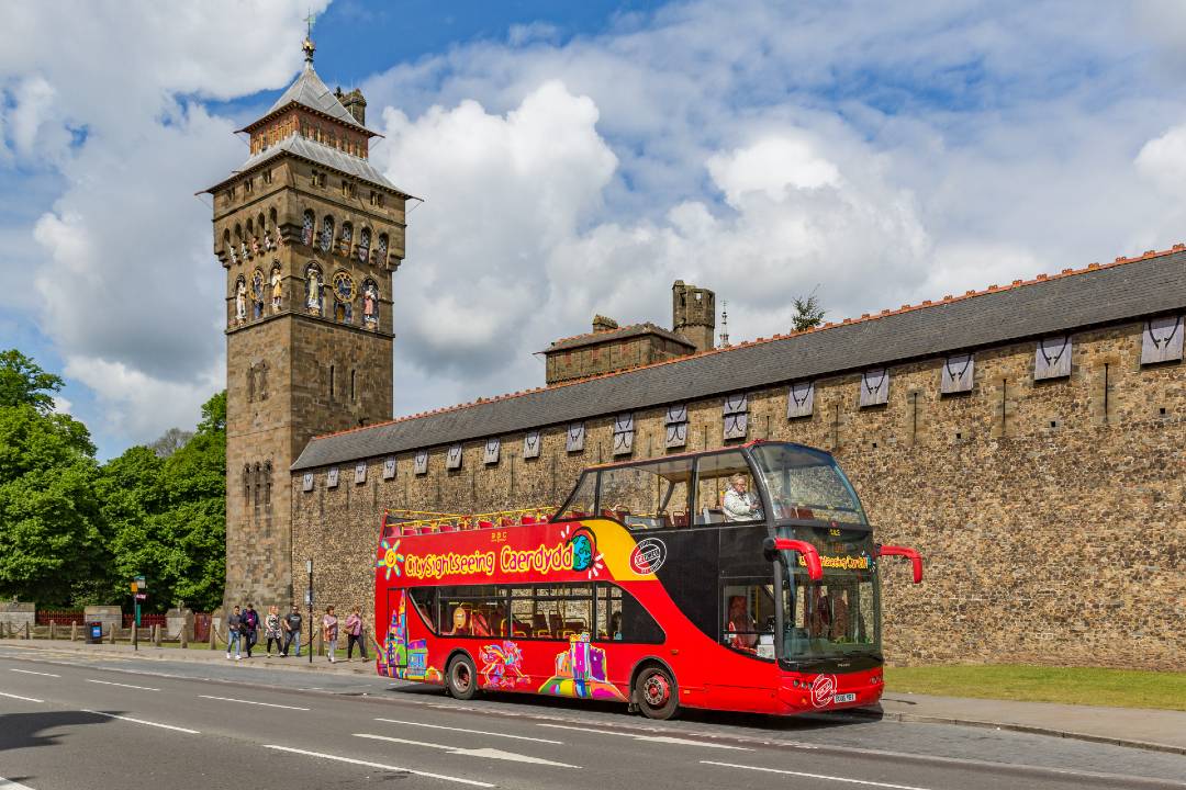 A Cardiff bus tour driving past an old building.