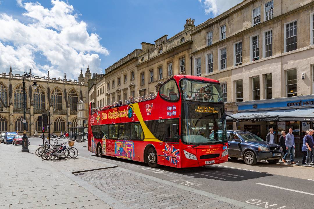 An open-top hop-on hop-off Bath bus tour driving through the streets.