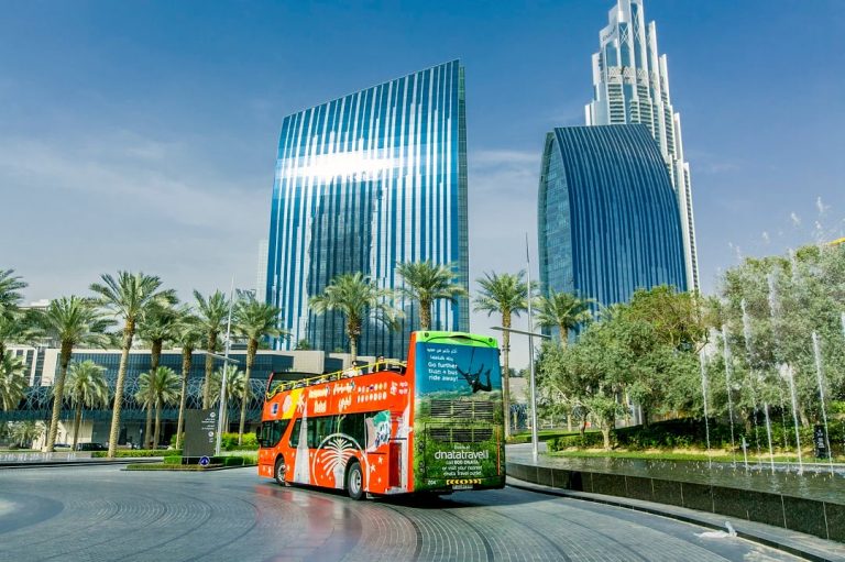 A red Dubai hop-on hop-off bus tour driving past Boulevard Plaza.