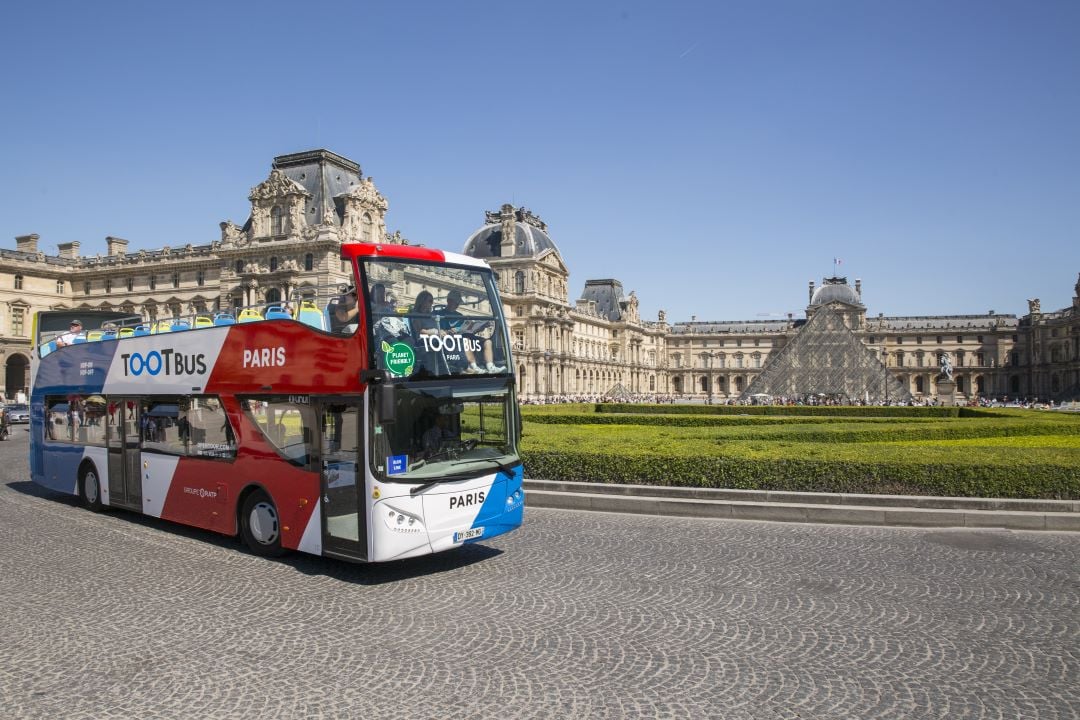 An open-top bus tour driving past the Louvre Museum.