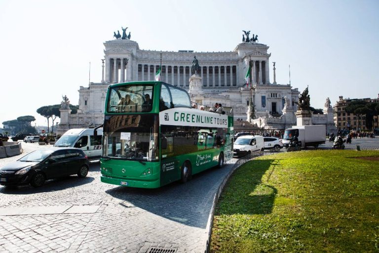 An open top bus in Rome parked in front of the Monument to Victor Emmanuel II.