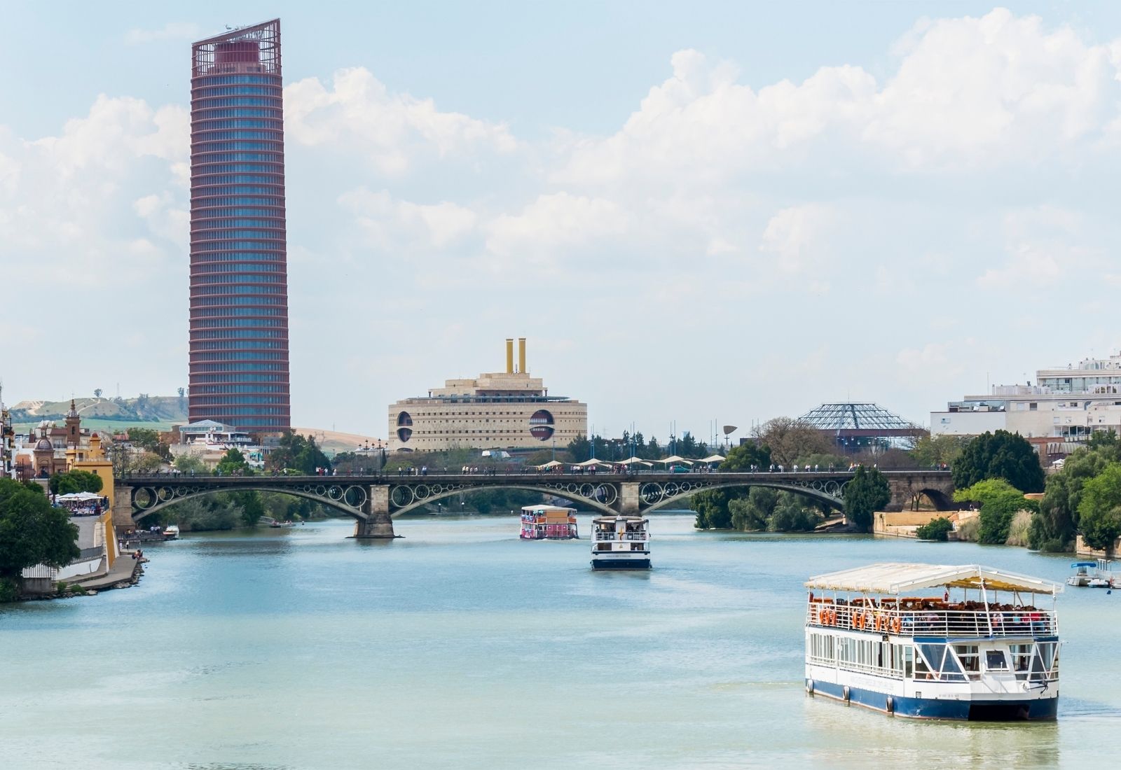 A photo of a boat on the Guadalquivir river, with the Sevilla Tower in the background.